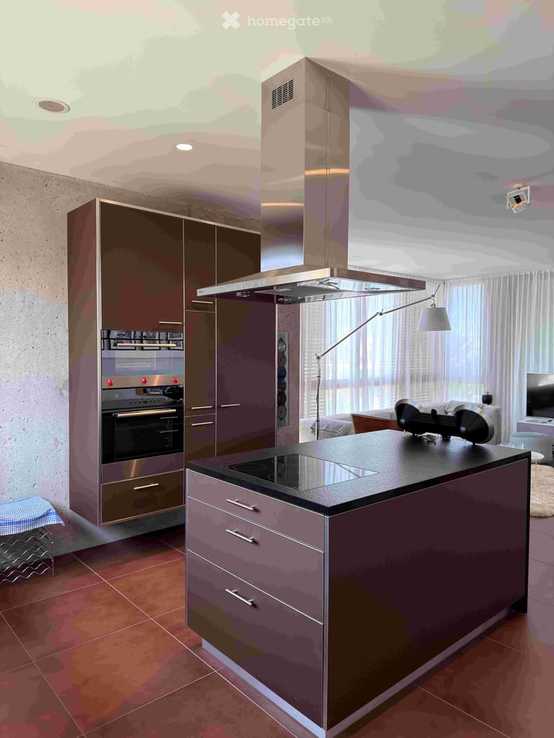 Modern kitchen with dark cabinets, stainless steel oven, island with induction cooktop, and a range hood. Features a large window with white curtains and a lamp on the island.