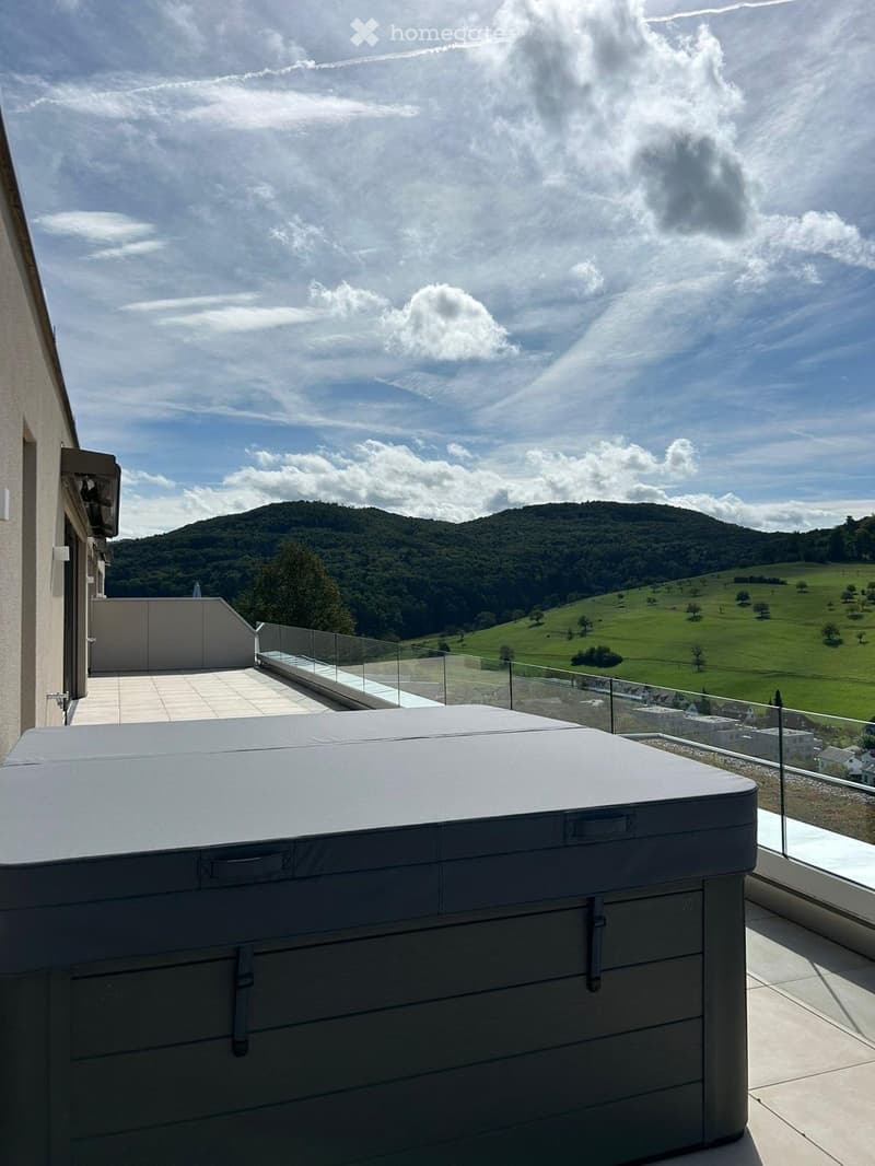 Balcony with a hot tub, glass railing, and scenic mountain view.