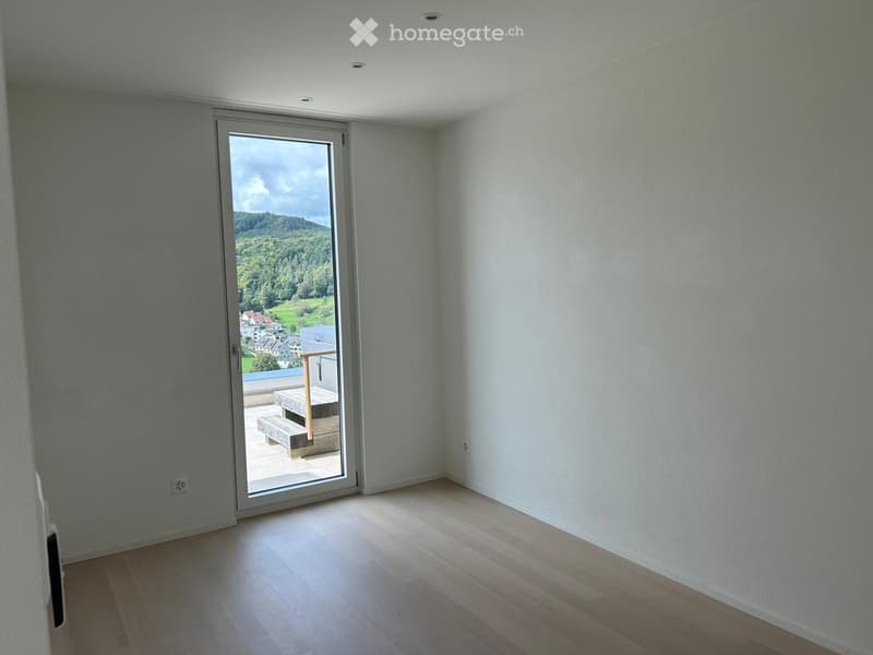 Empty room with light wooden flooring, white walls, and a large sliding glass door leading to a balcony with outdoor seating.