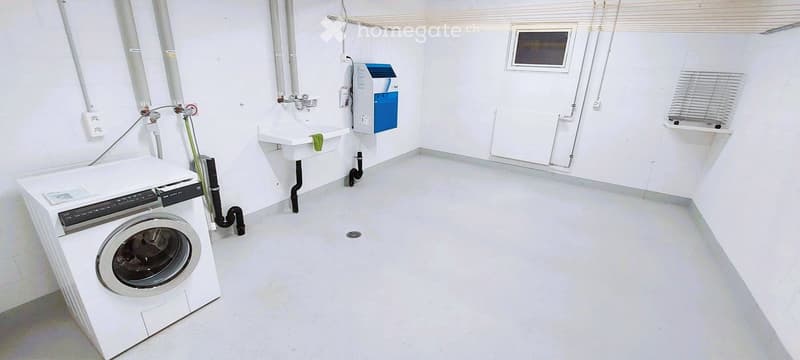 Clean, white-walled bathroom with a washing machine, sink, and water heater. The floor is smooth and white.