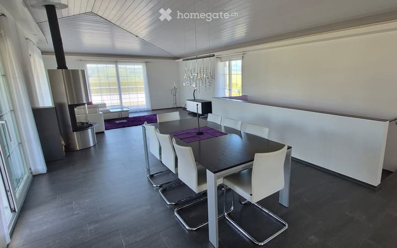Modern dining and living area with a sleek black dining table, white chairs, a cozy sofa, a contemporary fireplace, and a chandelier hanging from the ceiling.