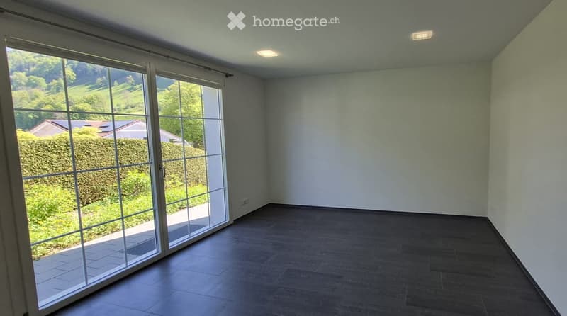 Empty room with large sliding glass doors leading to an outdoor area, dark tiled floor, and white walls.