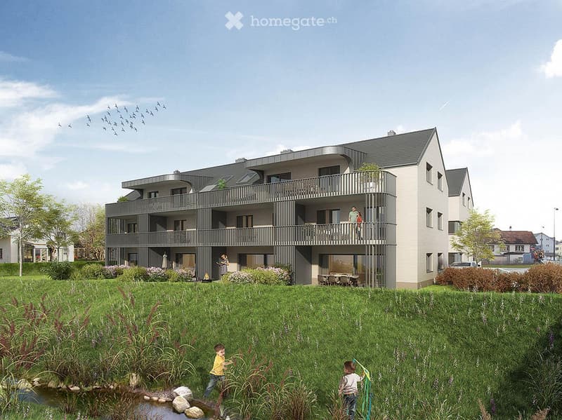 Modern multi-story residential building with balconies, surrounded by a green lawn and small water feature.