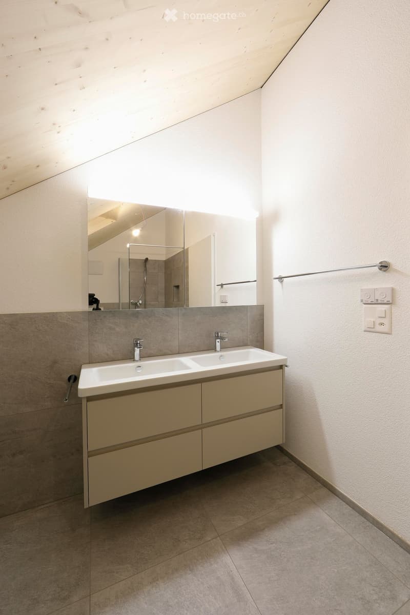 Modern bathroom with a double sink, sleek cabinetry, large mirror, and tiled walls.