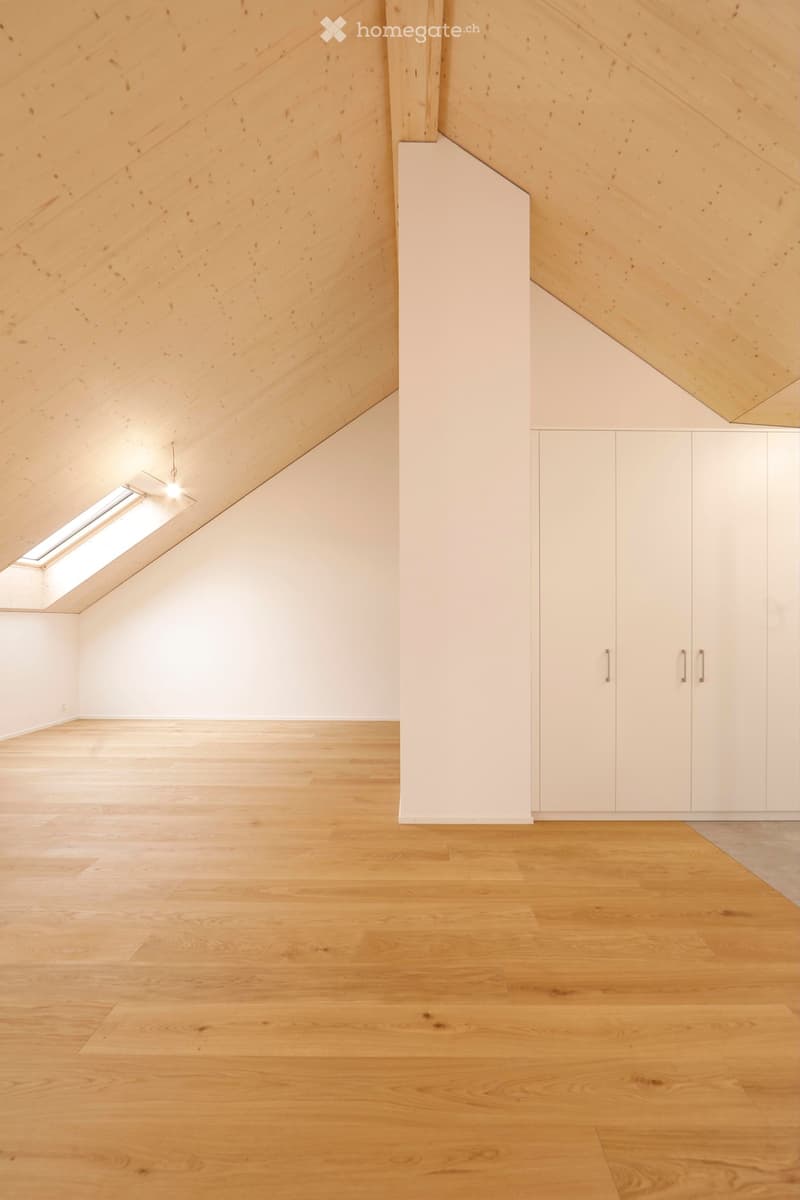 An attic room with wooden floors, white walls, a skylight window, and a wooden beam ceiling.