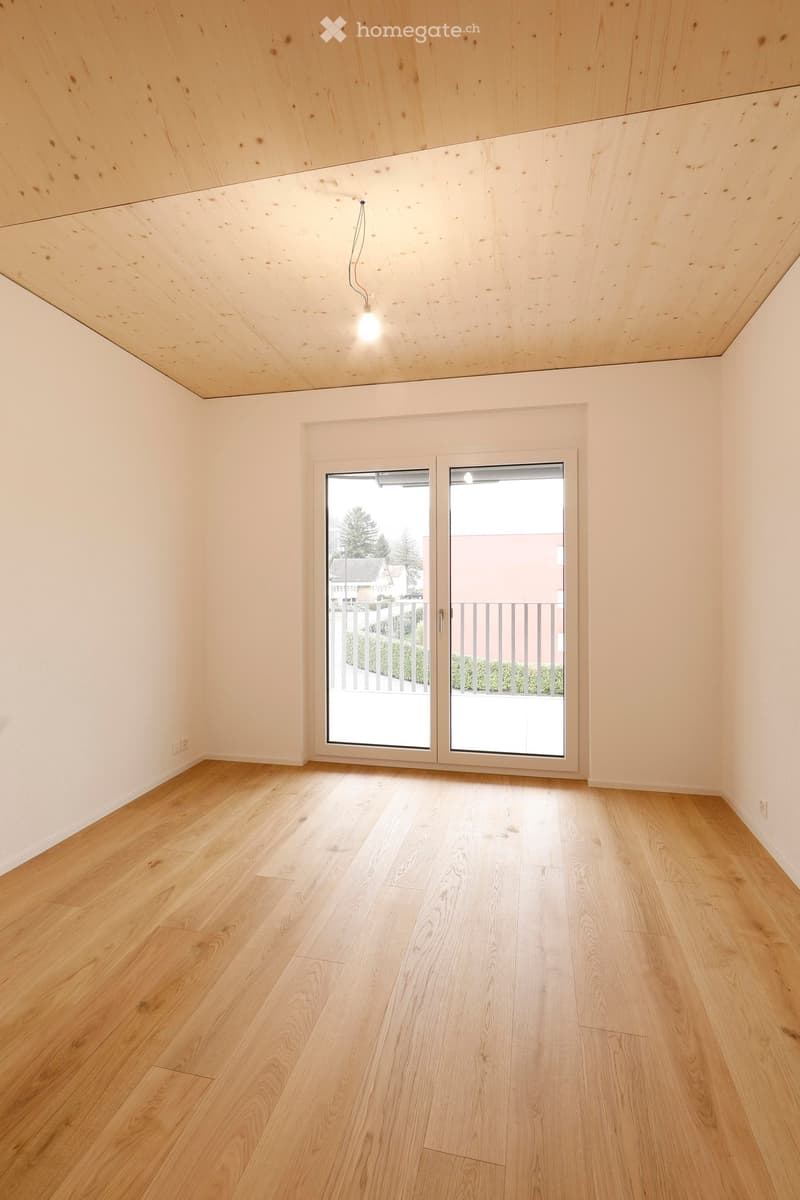Light colored hardwood floors, sliding glass doors to balcony, white walls, no furniture