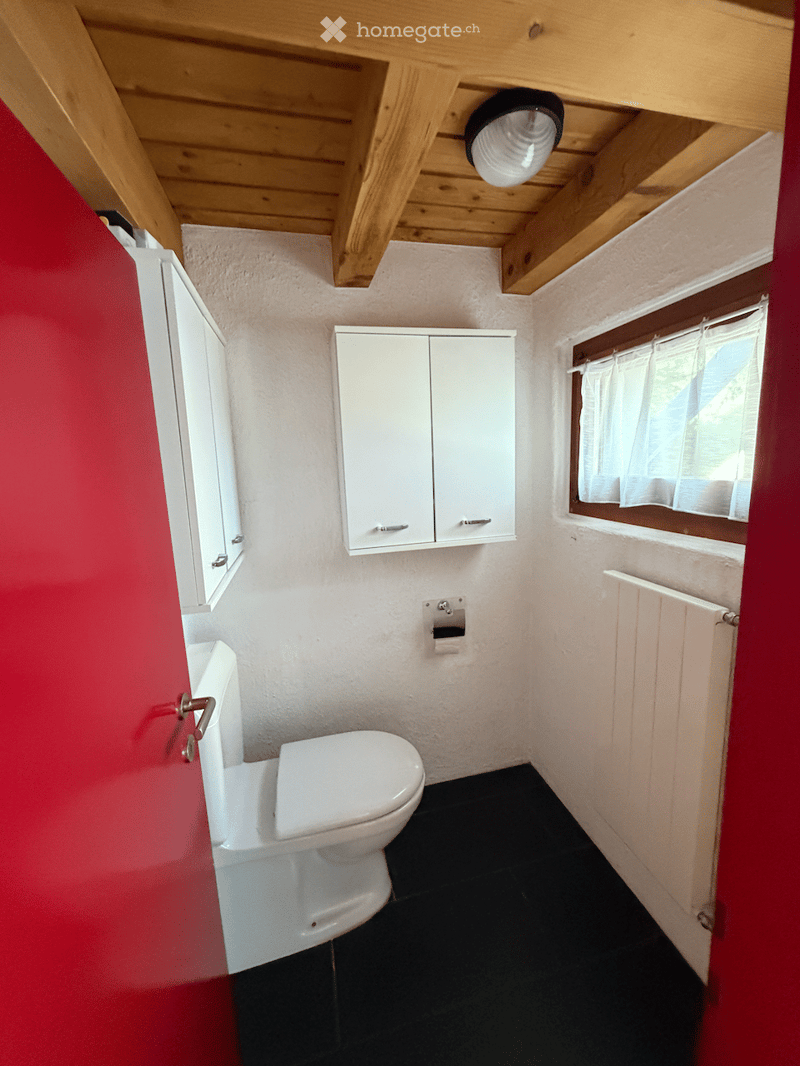 Compact bathroom with white toilet, white cabinets, black tiled floor, and a window with white curtains.