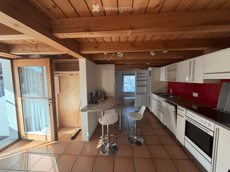 Modern kitchen with white cabinets, stainless steel appliances, island with bar stools, and exposed wooden ceiling beams.