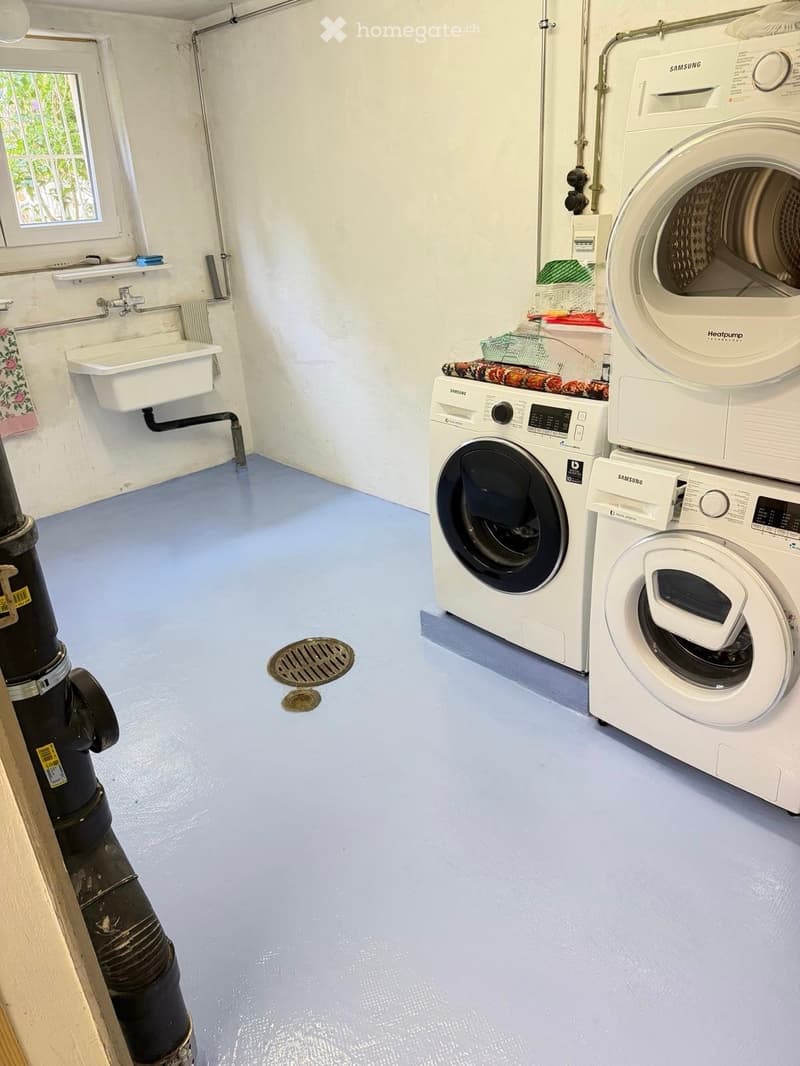 Bathroom with a sink, faucet, and stacked washing machine and dryer. Blue floor and white walls.