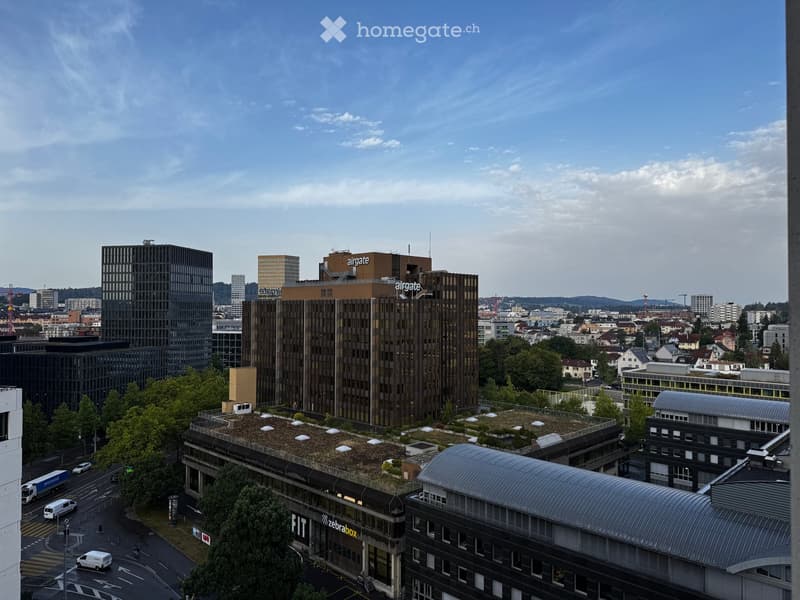 A panoramic view of a cityscape with modern buildings, including a prominent structure labeled "airgate" and a building with a green roof. The scene includes roads, vehicles, and surrounding greenery.