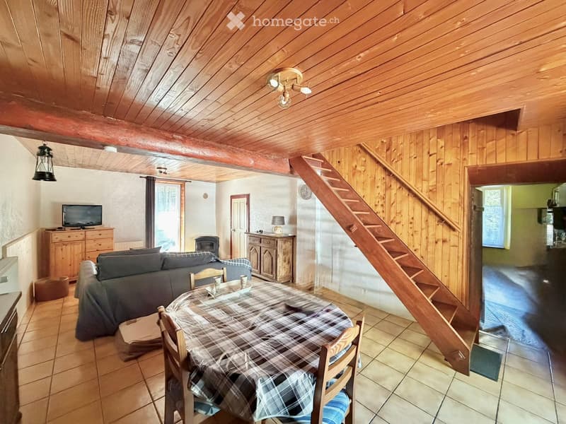 Cozy living room with wooden beams, a sofa, dining table, chairs, TV, and a staircase leading to another level.