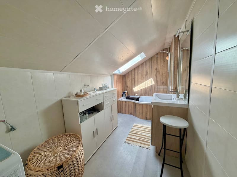 Modern bathroom with a skylight, white cabinets, a sink, a bathtub, and a wicker stool.