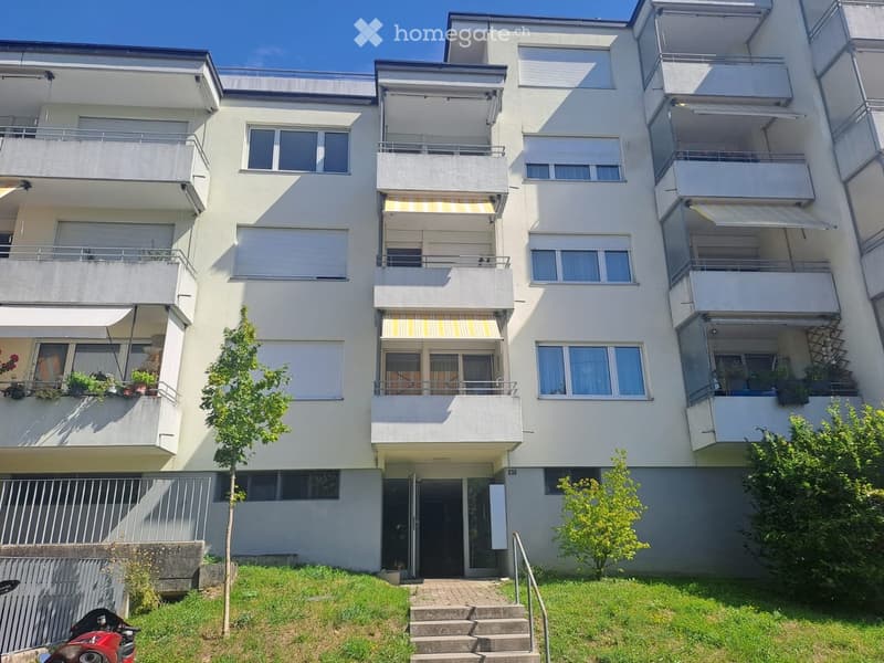 Multi-story residential building with balconies, large windows, and a staircase leading to the entrance.