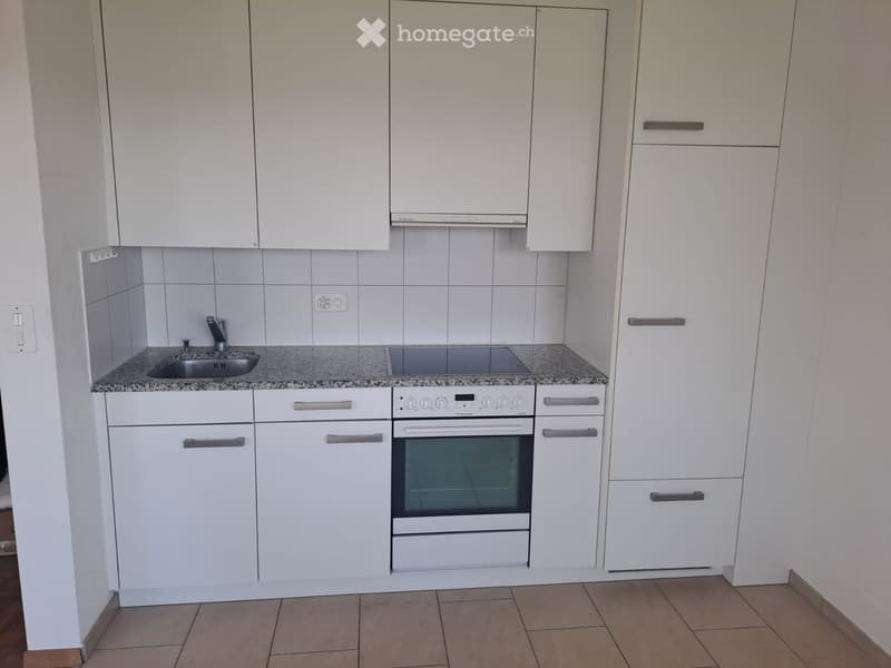 Compact kitchen with white cabinets, granite countertop, sink, and built-in oven.
