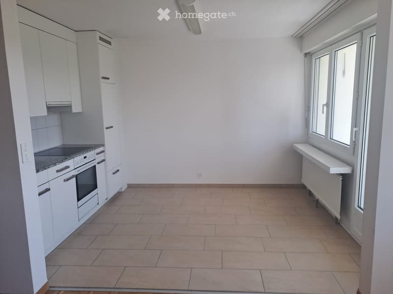 Modern kitchen with white cabinets, a built-in oven, and a tiled floor. The space is bright with large windows and a radiator under the windows.