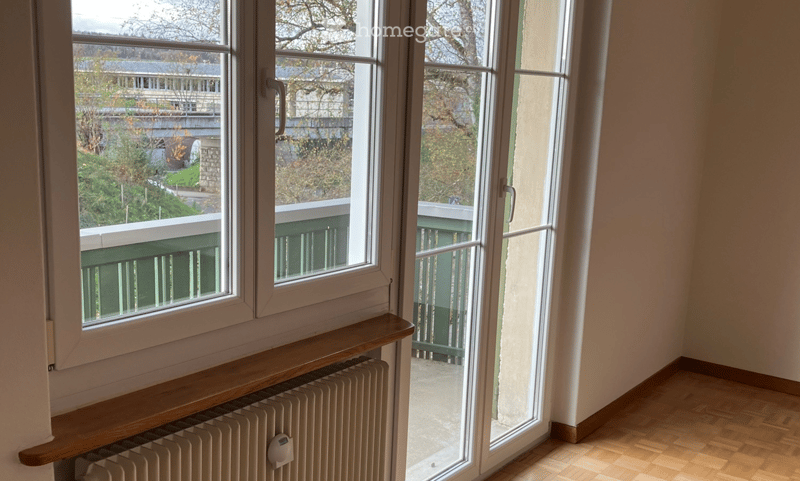 Empty room with wooden flooring, large windows, radiator, and access to a balcony.