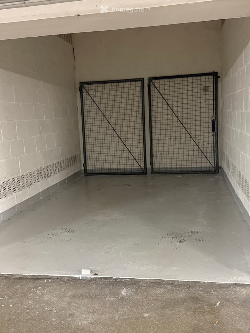 Empty garage with concrete floor, white brick walls, and a metal gate.