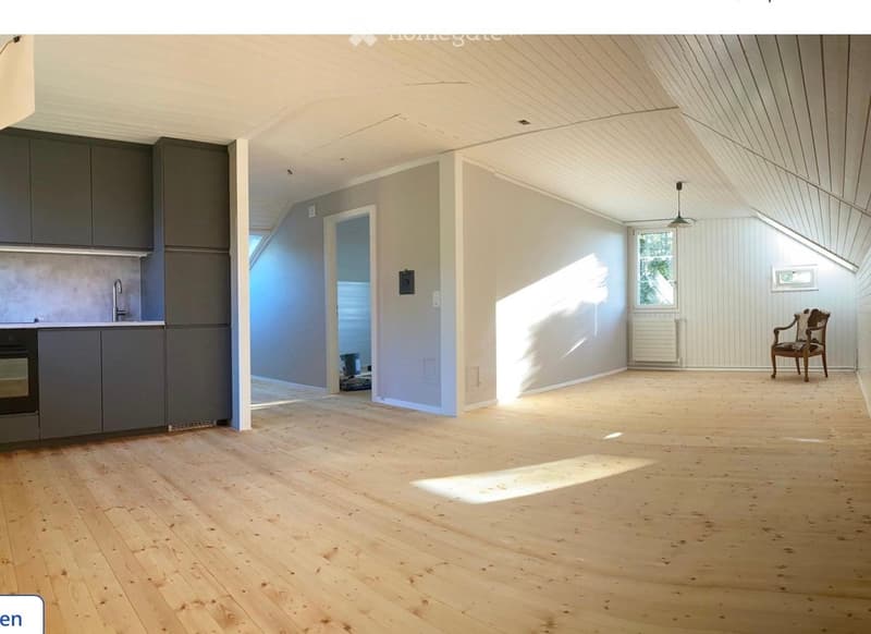 Bright, open room with wooden flooring, grey cabinets, and a single wooden chair near a window. Sunlight streams in, casting shadows on the floor.