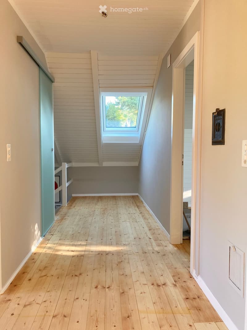 Bright hallway with wooden flooring, white walls, and a skylight window at the far end. Features a built-in shelf on the left and a door on the right.
