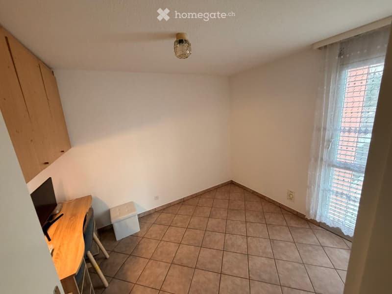 empty room, white walls, wooden flooring, ceiling lamp, desk with monitor, small bench, window with curtains