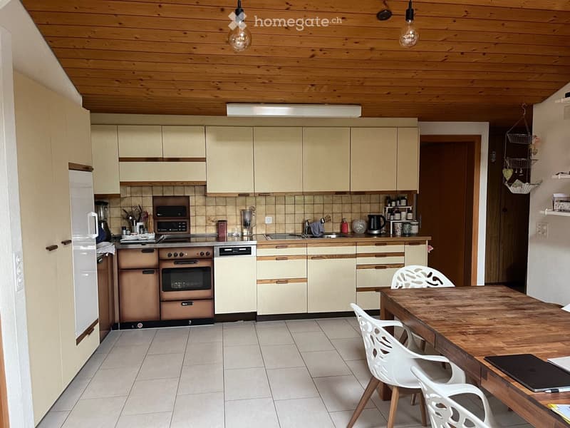 Modern kitchen with light wood cabinets, stainless steel appliances, and a wooden dining table with white chairs.