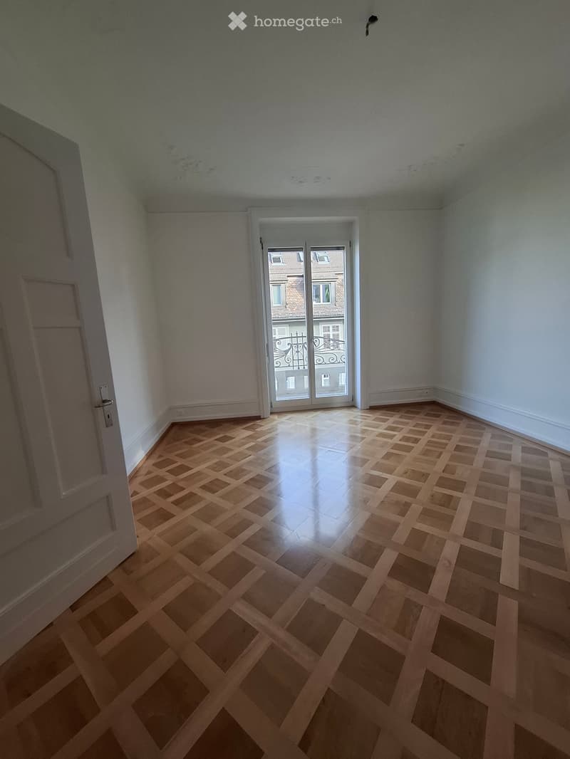 Empty room with wooden parquet flooring, white walls, and a sliding glass door leading to a balcony.