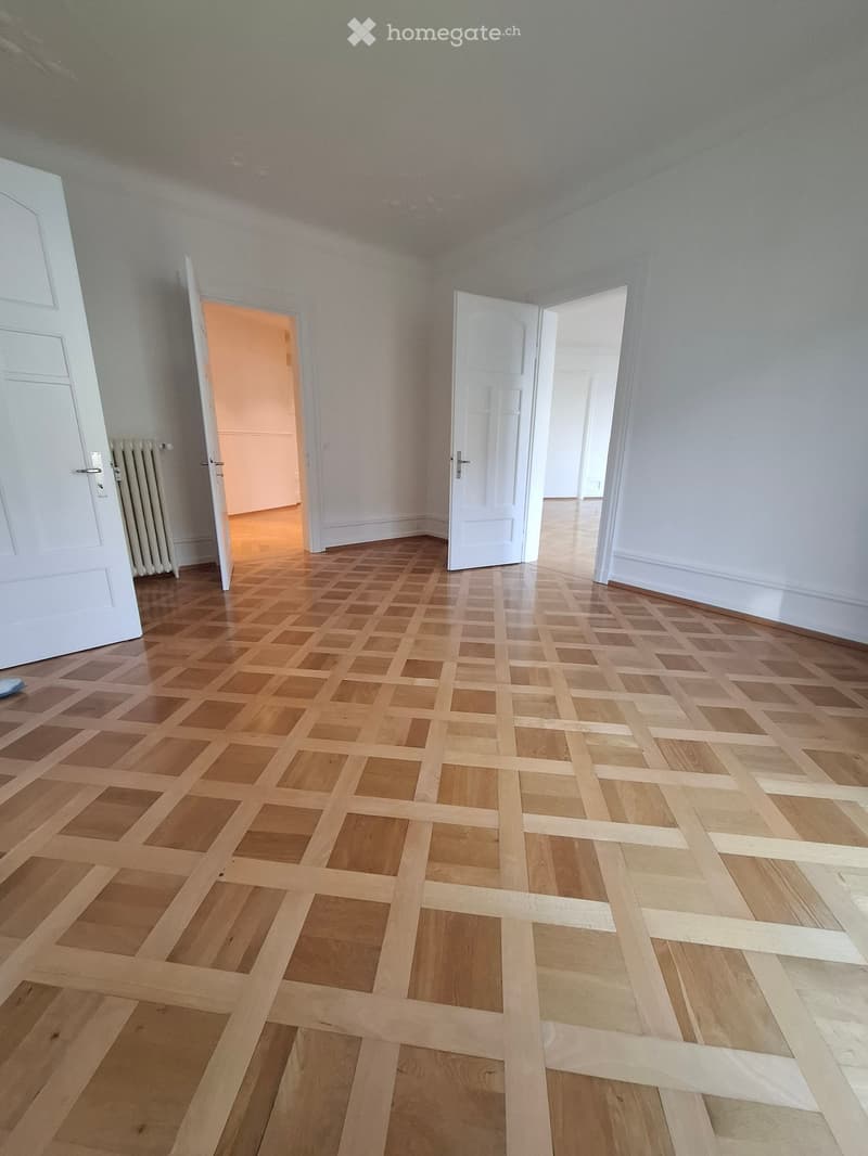 Empty room with wooden parquet flooring, white walls, and multiple open doors leading to other spaces.