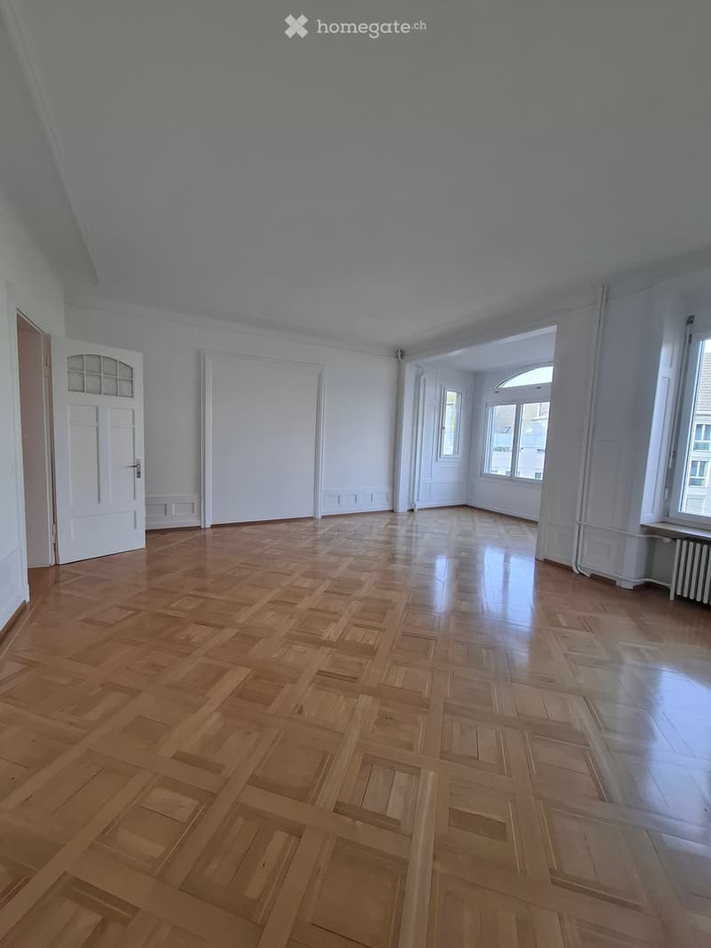 Empty room with wooden parquet flooring, white walls, and large windows. No furniture or equipment visible.