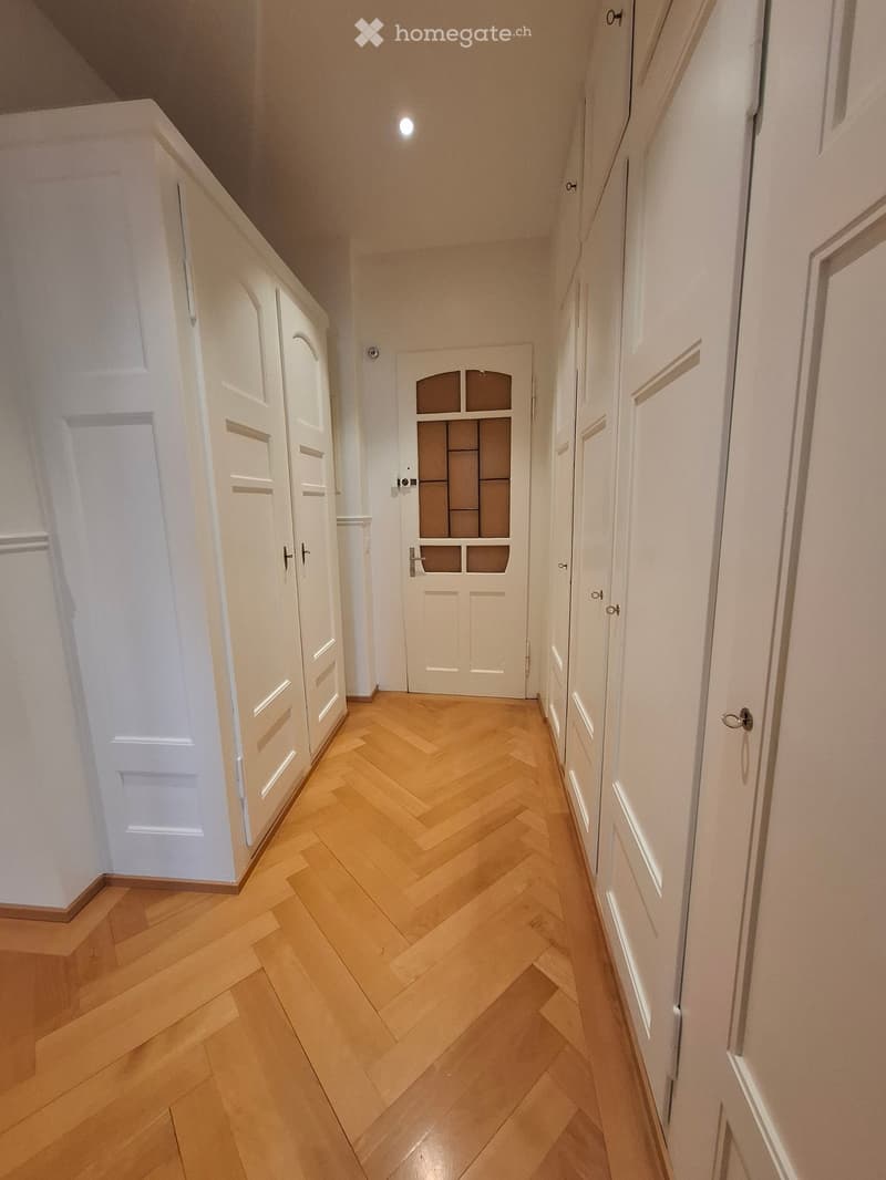 A narrow hallway with herringbone-patterned wooden flooring, white walls, and multiple white doors with glass panels.