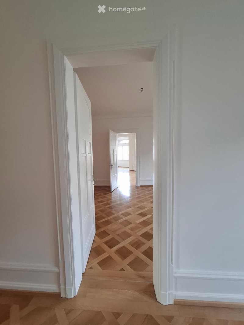 Empty hallway with wooden flooring and white walls, featuring open doors leading to other rooms.