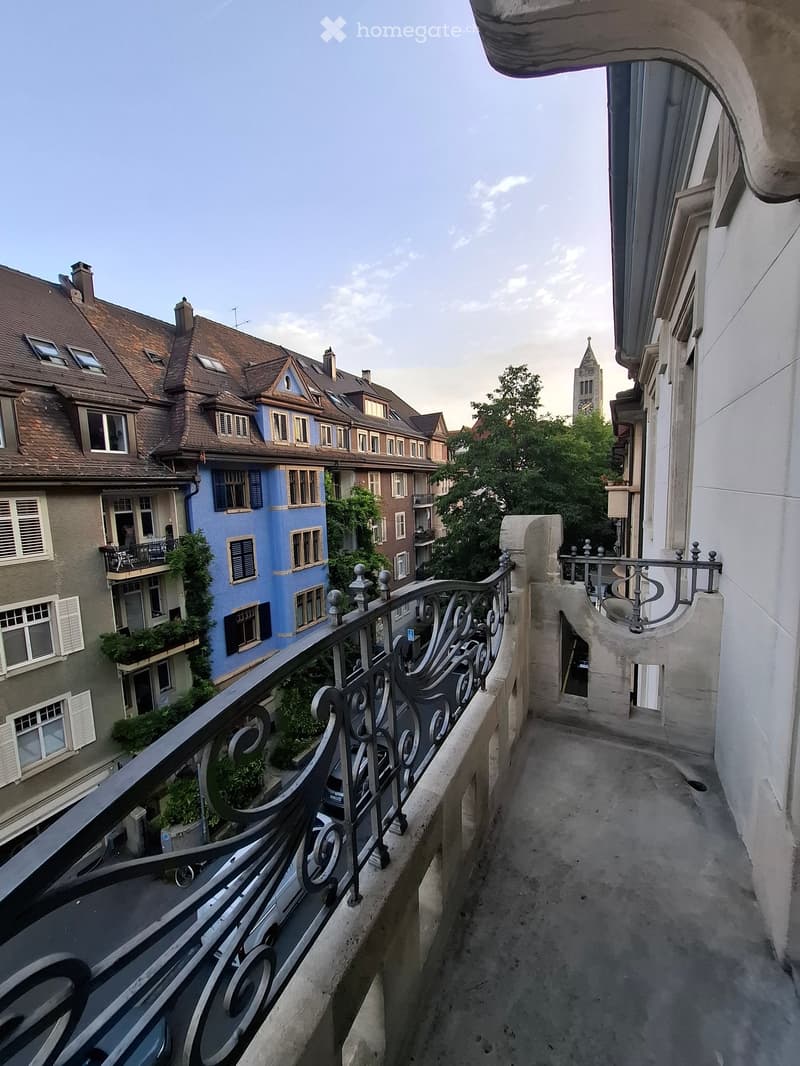 Balcony with ornate metal railing overlooking a street lined with colorful residential buildings and a church tower in the background.