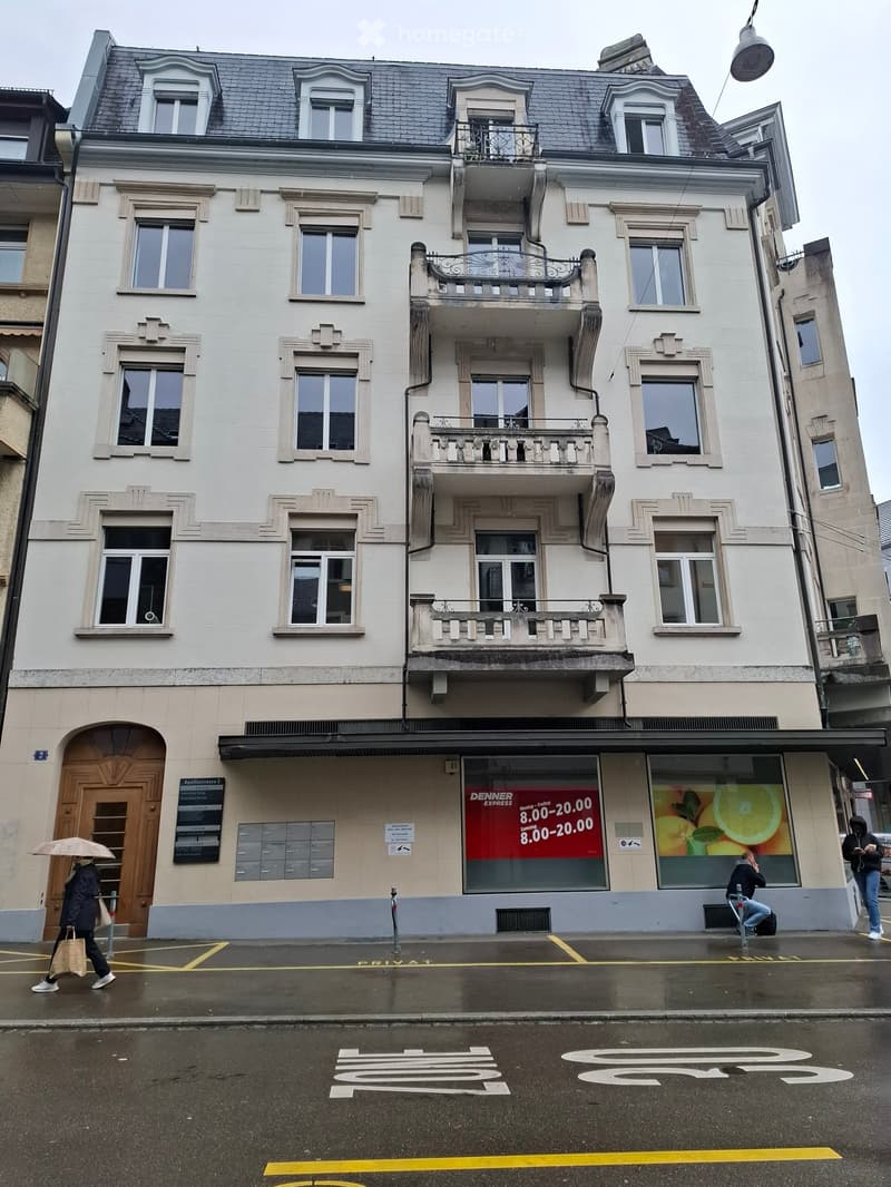 4 story white building with multiple balconies, storefronts, ground floor access door