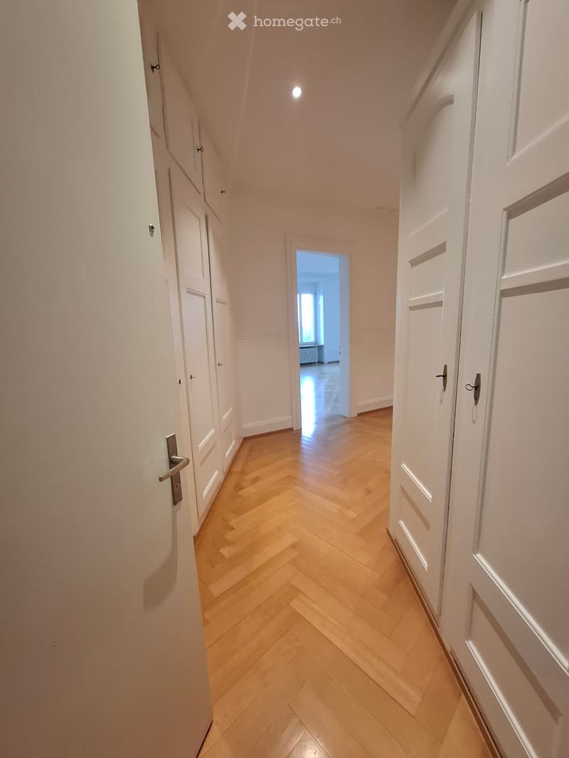 A narrow hallway with light wooden herringbone flooring, white walls, and multiple closed white doors on both sides.