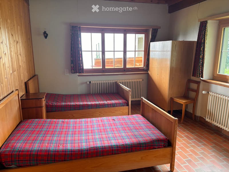Cozy bedroom with two single beds, wooden furniture, and large windows with curtains.
