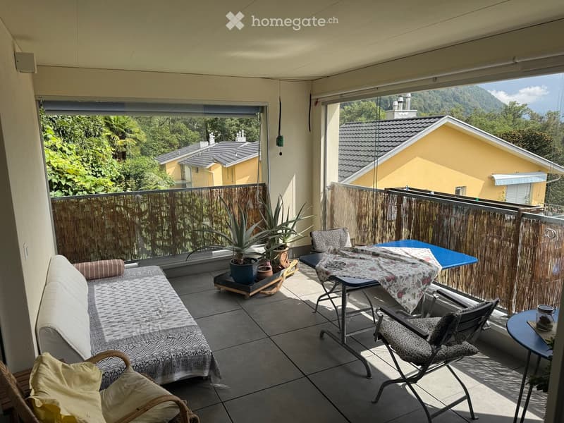 Balcony with tiled floor, sofa, table, chairs, potted plants, and scenic mountain view.