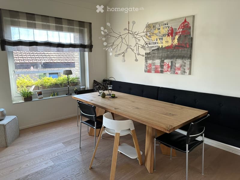 Modern dining area with a wooden dining table, four chairs, a bench seating area, a pendant light fixture, and a large window with a view of the roof.