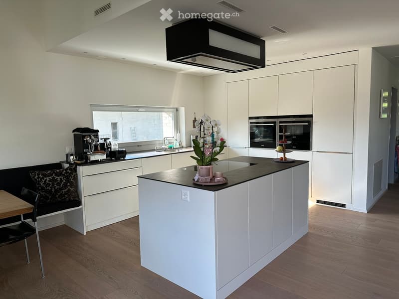 Modern kitchen with white cabinets, black countertop, island, coffee machine, sink, and seating area with bench and chair.