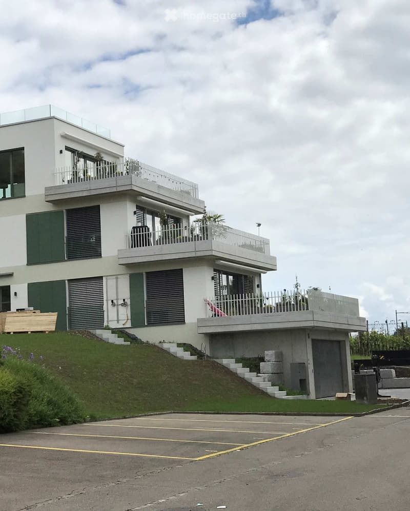 Modern two-story house with white exterior, green shutters, multiple balconies, and a raised ground floor accessed by steps.