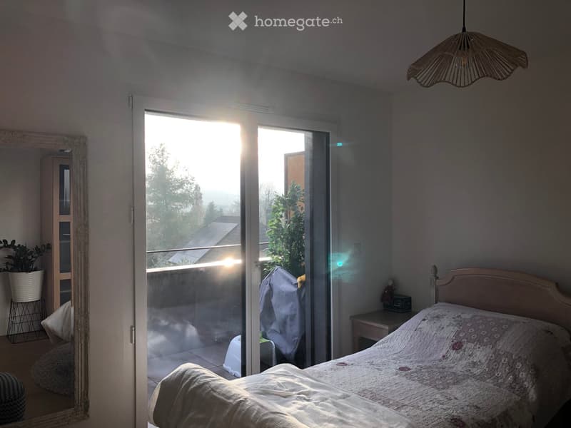 Bright bedroom with a double bed, nightstand, large mirror, and a sliding glass door leading to a balcony.