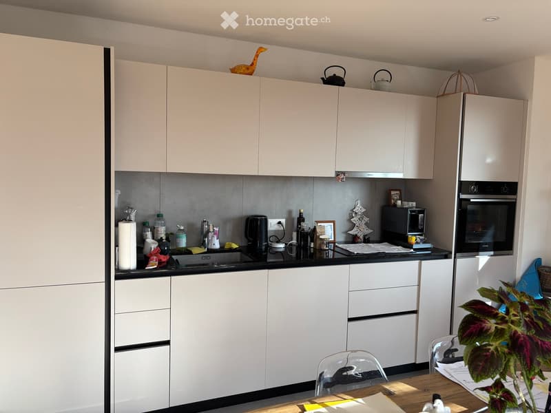 Modern kitchen with white cabinets, black countertop, sink, oven, microwave, coffee maker, and a small dining area with a table and chair.