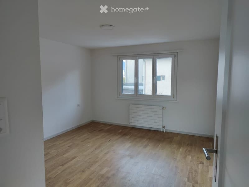 Empty room with wooden flooring, white walls, a window with three panes, and a radiator below the window.