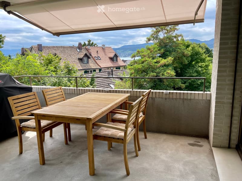 Balcony with table and chairs, awning, covered by trees and lake view