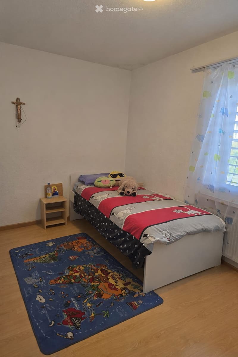 Cozy bedroom with a single bed, colorful bedding, a nightstand with a picture frame, a small rug, and a window with a curtain.