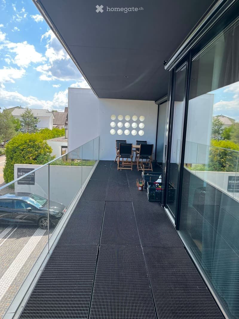 Modern balcony with dark tiled floor, glass railing, and a small seating area with a table and chairs.
