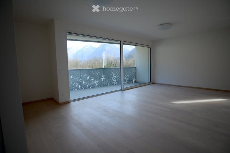 Empty room with wooden flooring, large sliding glass doors leading to a balcony with a mountain view.