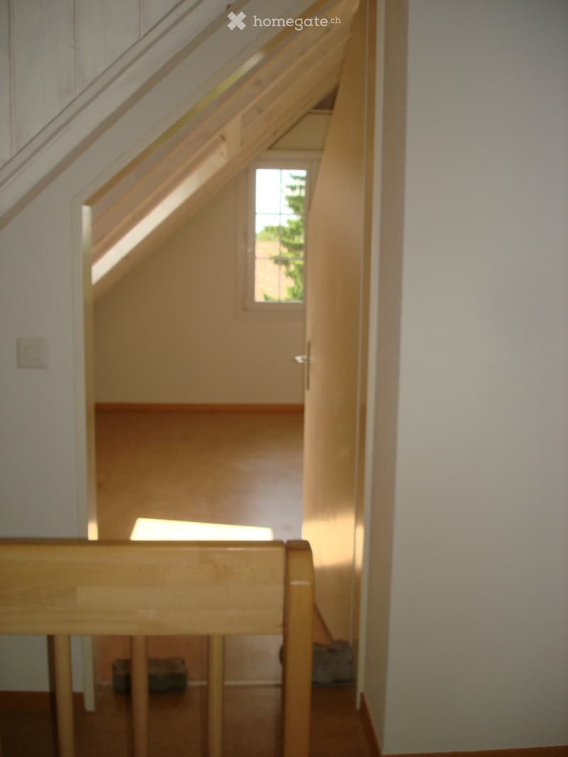 Wooden staircase with handrail and a small window at the top, leading to an upper level.