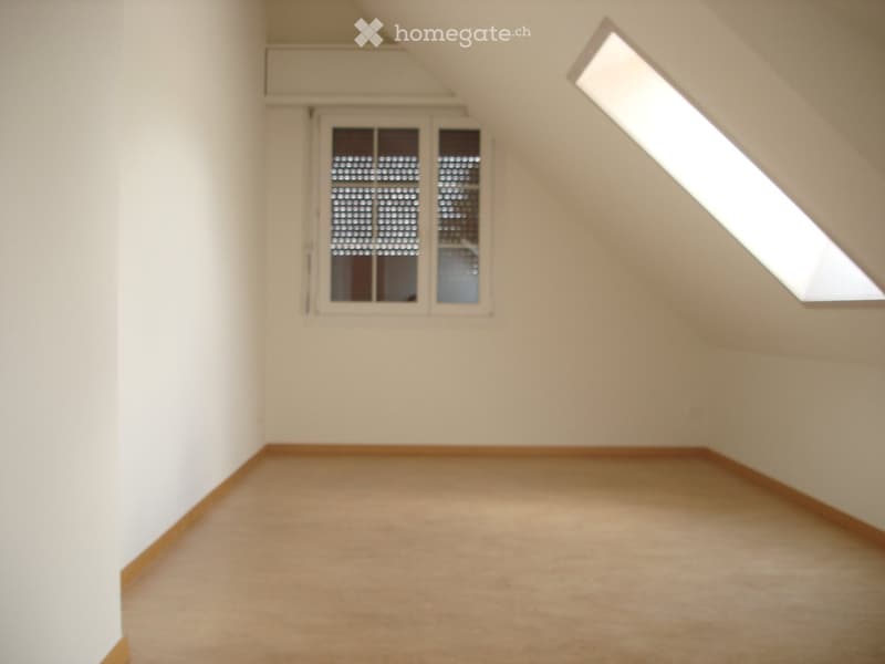 Empty attic room with sloped ceilings, carpeted floor, and two windows (one with blinds).