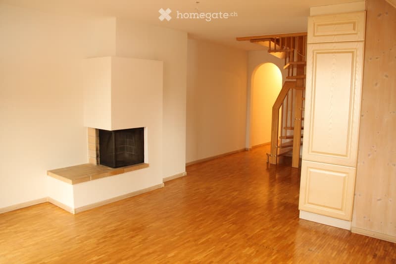 Empty room with wooden flooring, white walls, and a built-in fireplace. A staircase leads to another level.