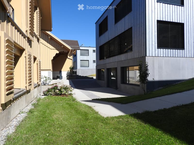 Modern buildings with concrete and metal facades, concrete walkway, small garden area, and a driveway