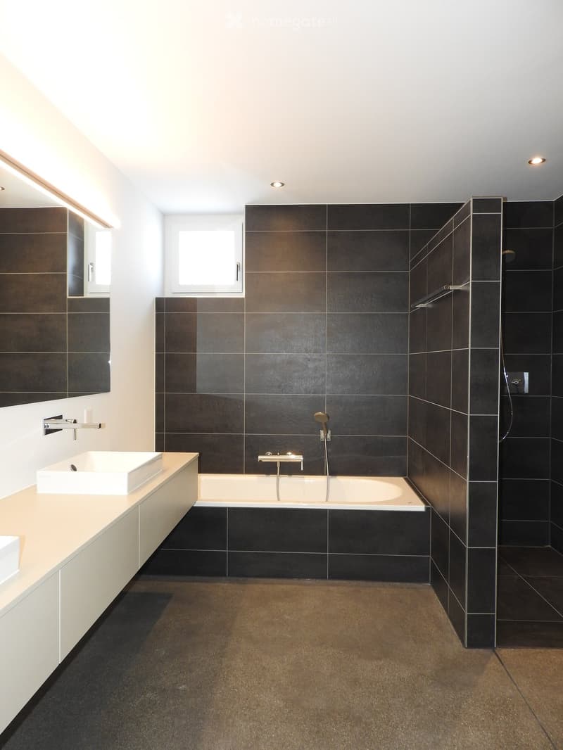 modern bathroom with black tiles, white bathtub, white sink, large mirror, walk-in shower